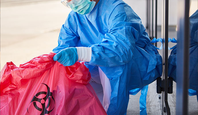 An expert in protective gear using a biohazard waste bag for cleanup