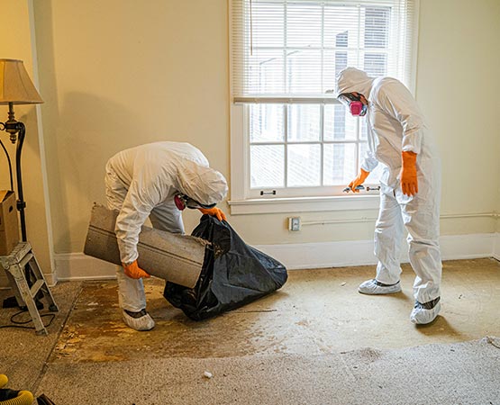 Two technicians in full white hazmat suits work in a room to remove contaminated flooring