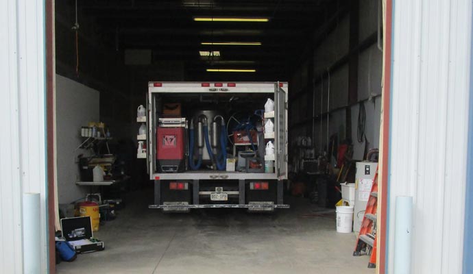 Rear doors of a truck-mounted system open, showing specialized equipment and supplies in a garage