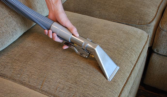 Expert cleaning upholstered couch with vacuum wand
