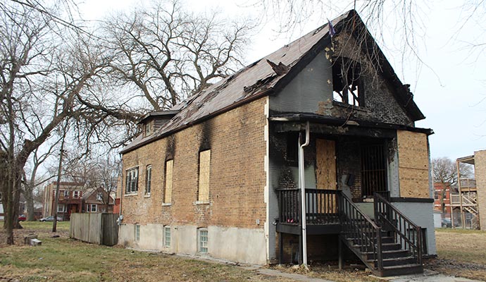 Fire-damaged brick house with boarded windows and smoke stains
