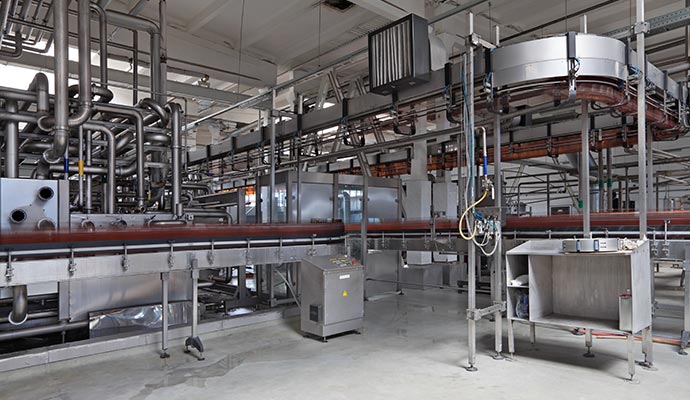 Interior of a food production facility featuring stainless steel machinery, pipes, and conveyor systems