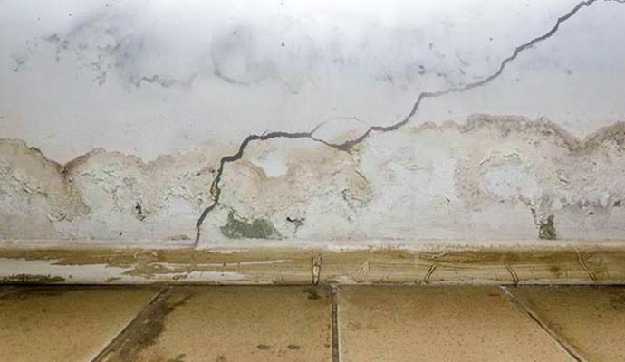 A low-angle shot of an interior wall where a large, jagged diagonal crack runs through the plaster