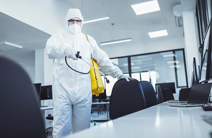 man in protective suit and face mask spraying for disinfection in the office