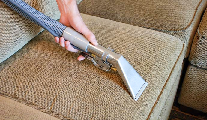 Person cleaning a beige sofa with an upholstery tool