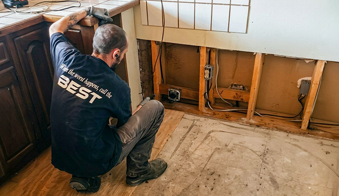 Restoration worker inspecting kitchen floor and exposed wall for restoration