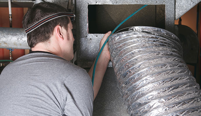 Technician guiding a hose into an HVAC duct system