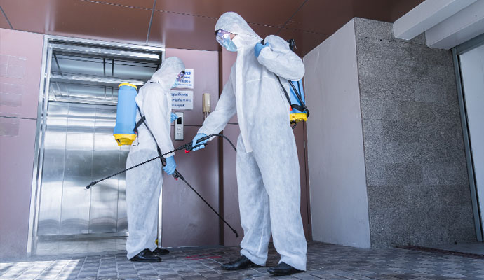Technicians in protective suits spraying disinfectant outside elevator