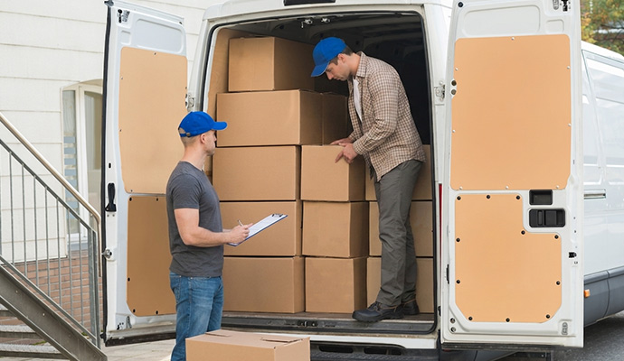 Two movers loading boxes into a van while checking a clipboard