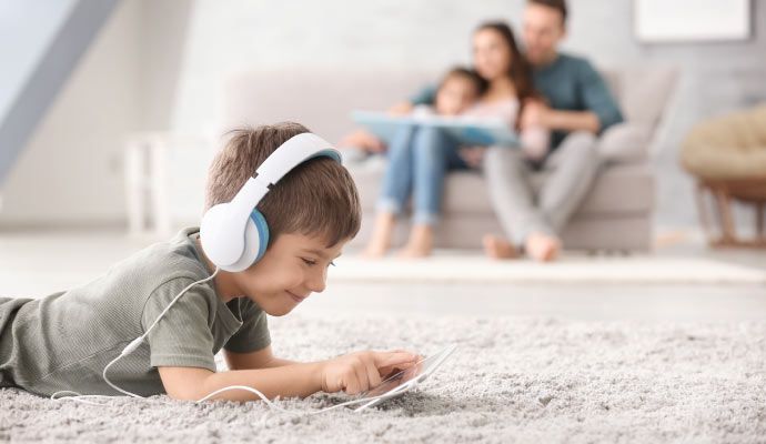 A boy laying on a clean carpet in a living room in front of his family