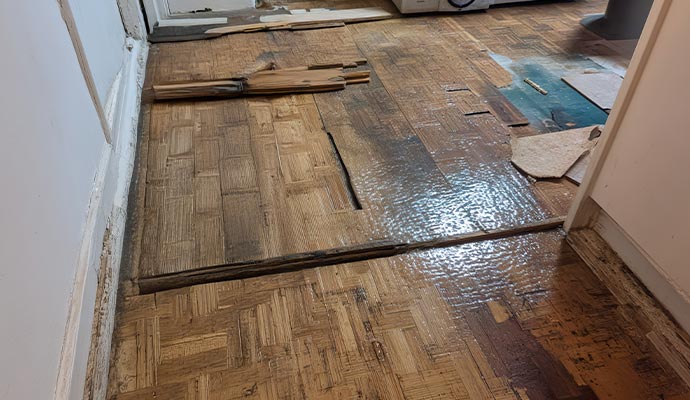 A high-angle view of a parquet wood floor showing water damage